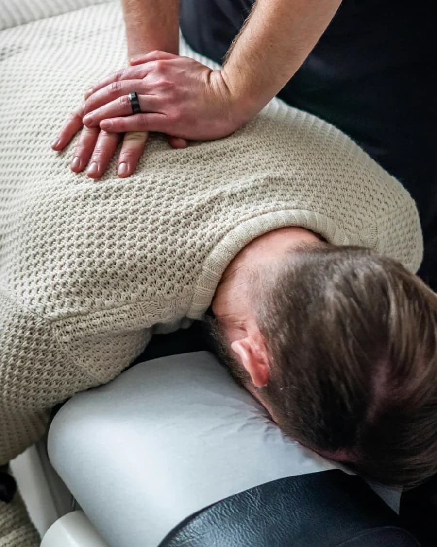 Chiropractor placing both hands on a patient upper back during a spinal adjustment