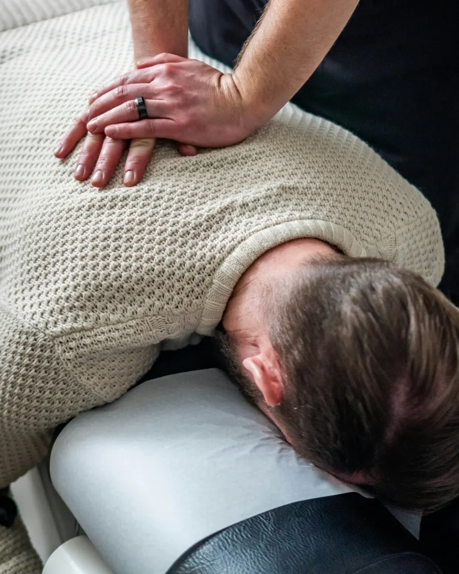 Chiropractor placing both hands on a patient upper back during a spinal adjustment
