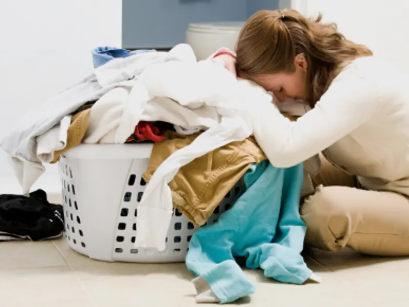 Woman kneeling and resting her head on a pile of laundry beside a laundry basket