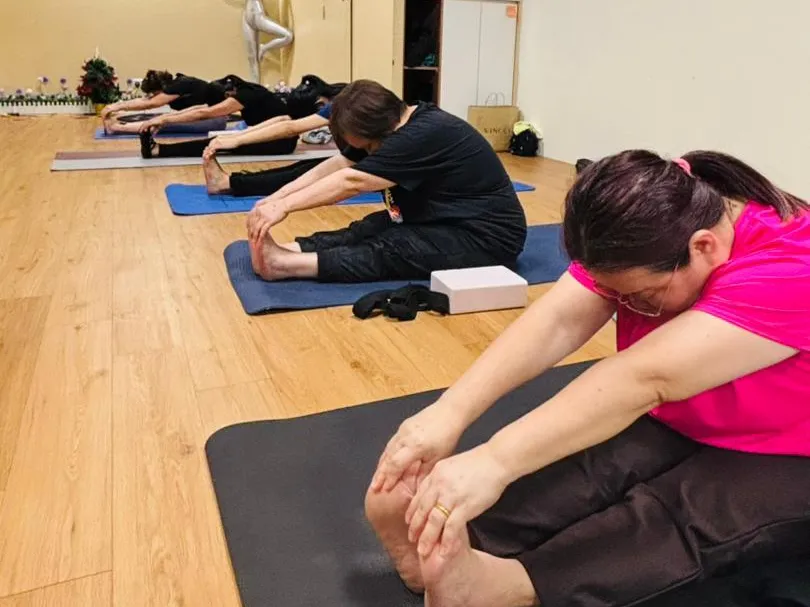 A row of students seated on mats reaching forward over their outstretched legs during a yoga class at Persistence Chiropractic Care in Cheras, Kuala Lumpur